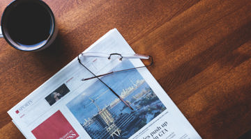 Newspaper, coffee and reading glasses on a wooden table