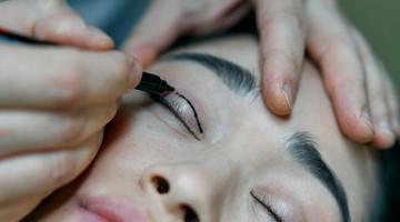 A person drawing a line on a young woman's eyelid