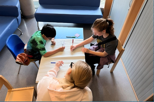 Three people of different ages siting around the table drawing on paper
