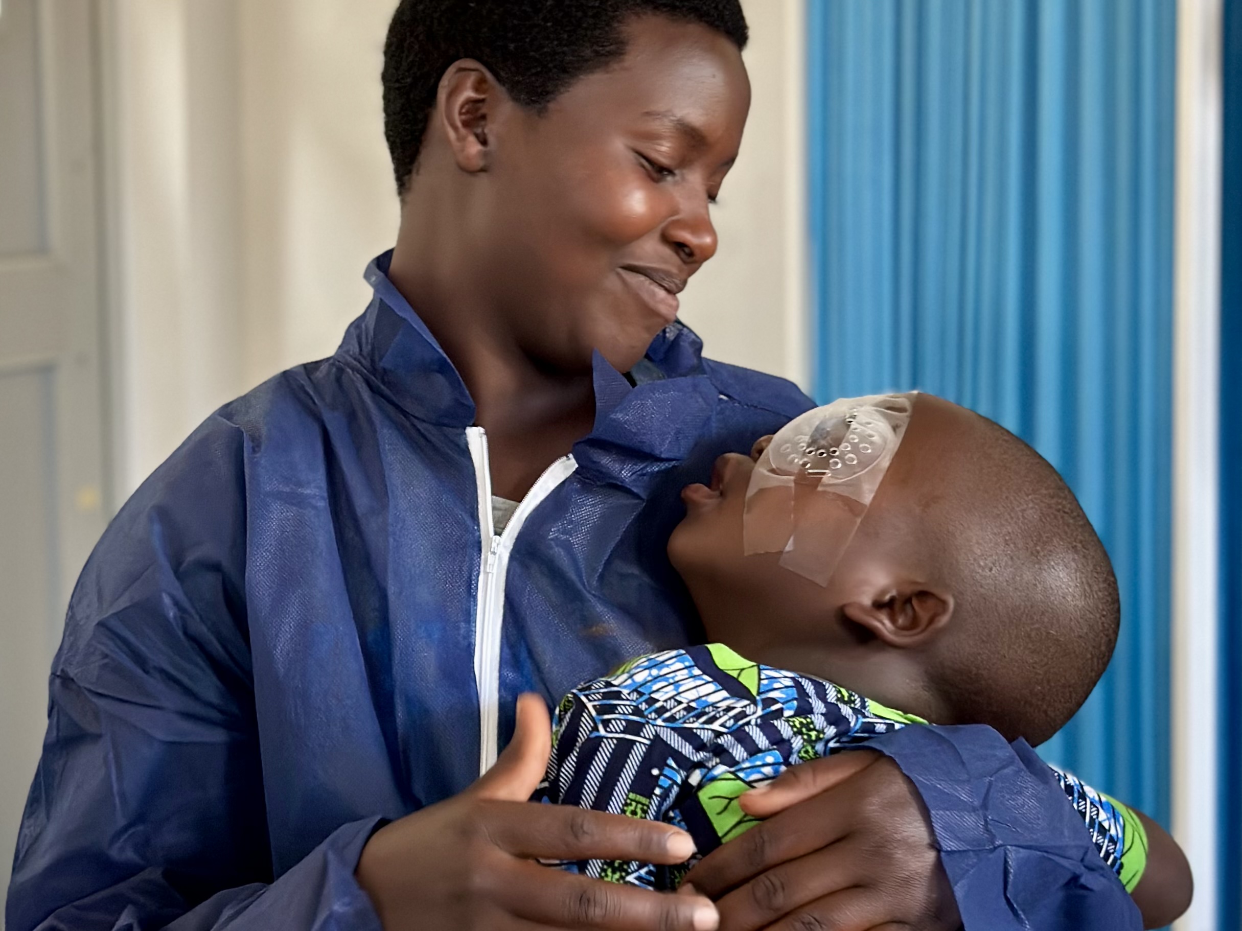 An adult affectionately cradling, and smiling, at a small child with an eye patch