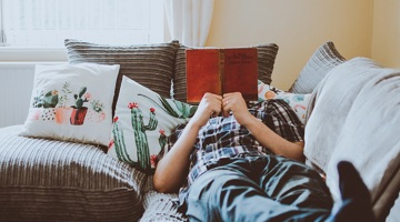 A man laying on the sofa reading a book