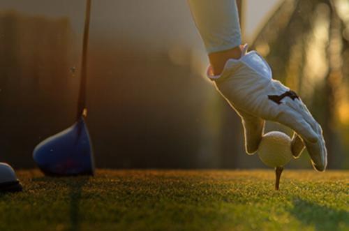 Gloved hand putting a golf ball on a tee, with a golf club next to it
