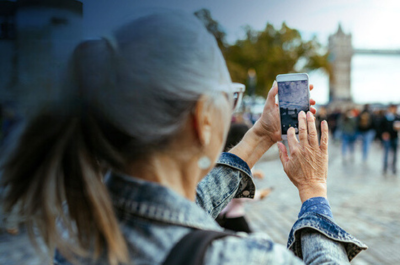 A mature woman taking a photo of a Tower Bridge