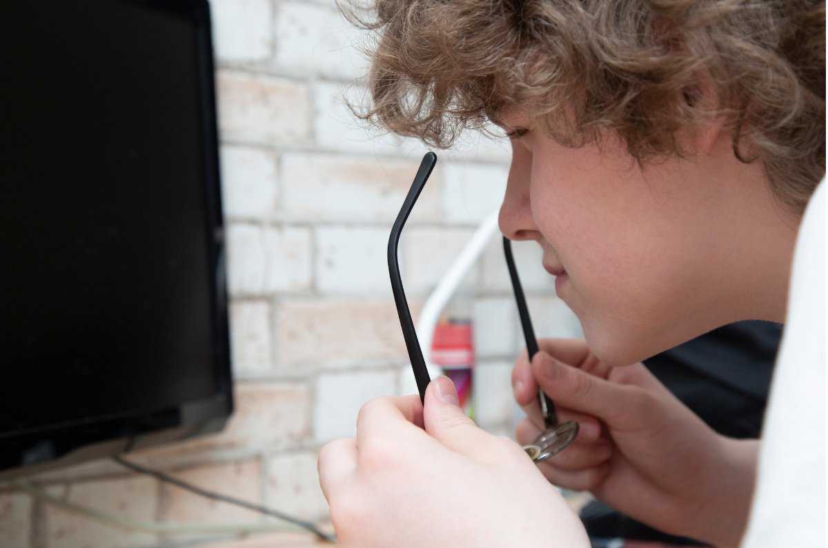 A child squinting and holding glasses in their hands when looking at the screen