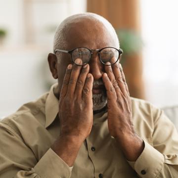 A mature man covering his eyes under his glasses